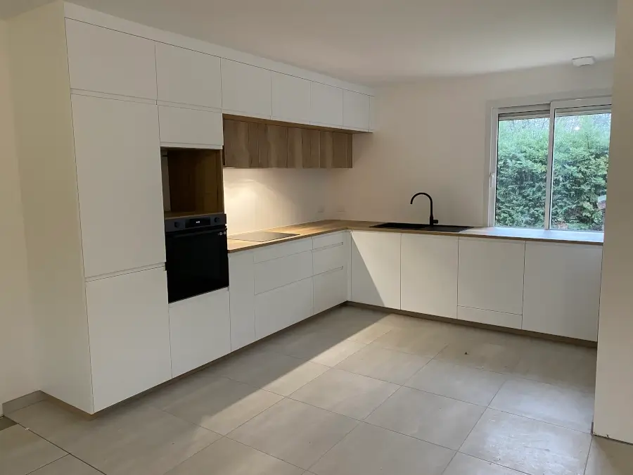 Imposante cuisine sur mesure blanche avec un vaste plan de travail en bois, offrant un espace de vie spacieux et élégant. Cette cuisine majestueuse combine l'esthétique lumineuse du blanc avec la chaleur naturelle du bois, créant une atmosphère accueillante et raffinée